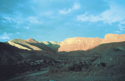 Un camino largo que baja y se pierde entre las sierras que el atardecer tiñe de un color rojo intenso.